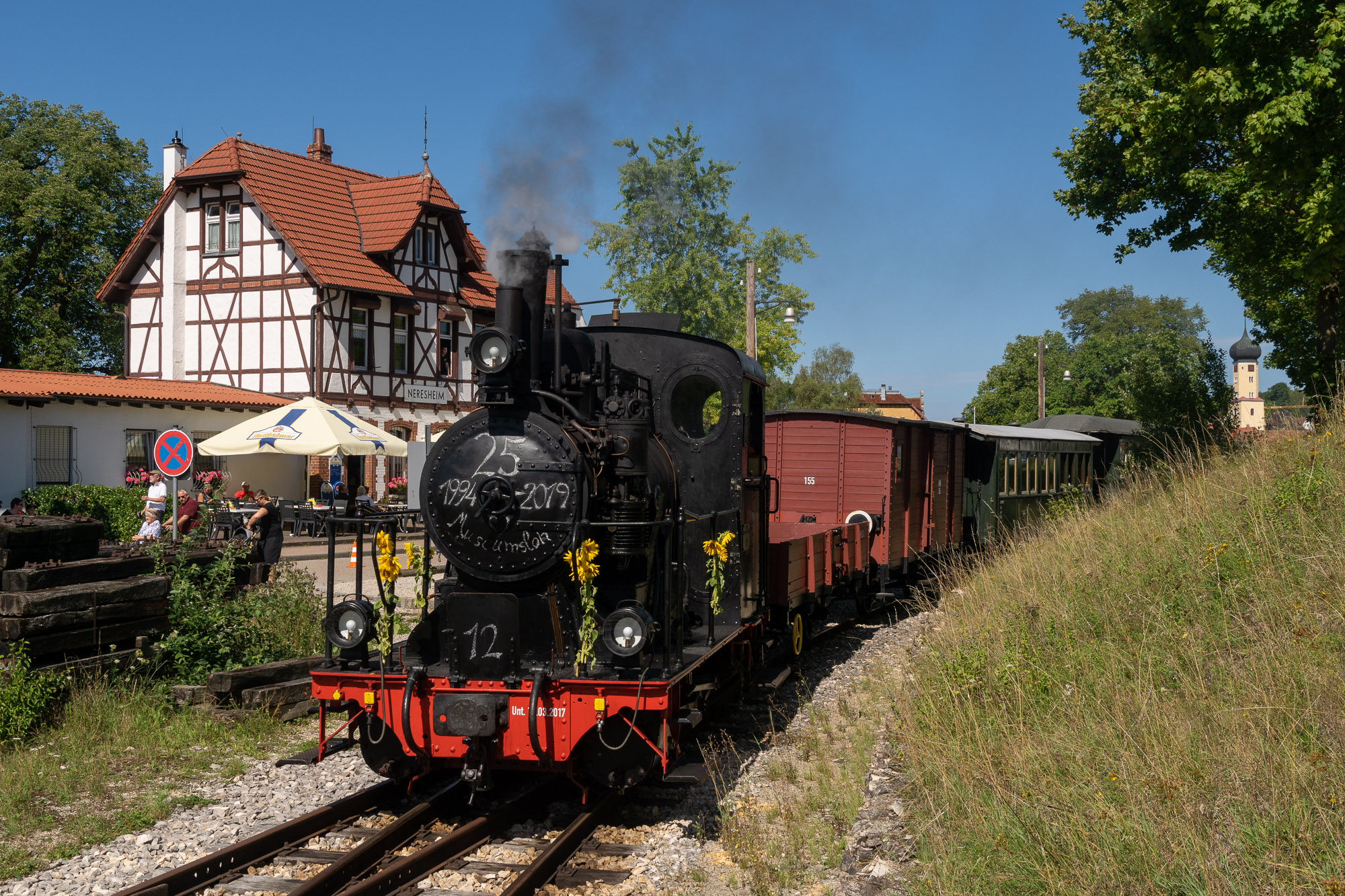 Lok 12 steht mit dem Personenzug vor dem Neresheimer Bahnhofsgebäude zur Abfahrt bereit